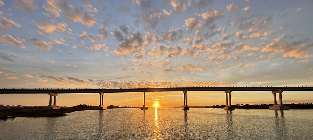 Soundside Park in Surf City, NC also offers some breathtaking views of the sunset each evening. This photograph, taken from one of the fishing platforms shows the sun settings beneath the highrise of Surf City Bridge, with the Hampstead area in the background.