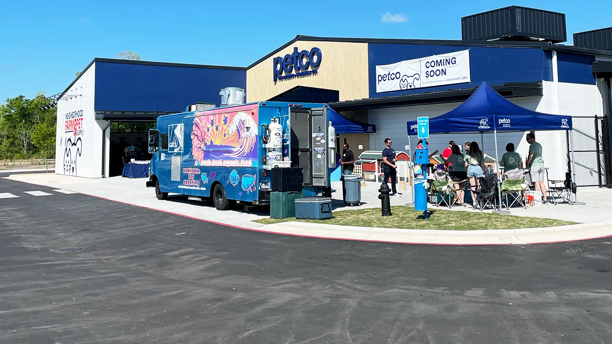 Petco storefront with a Coming Soon banner, a food truck, tents, and a crowd at the grand-opening event.