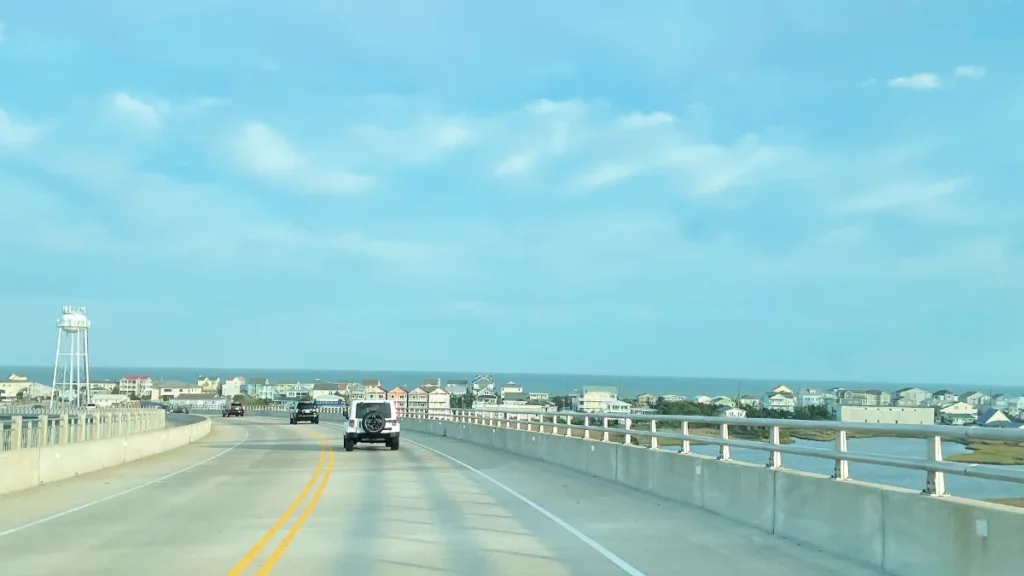 Driving down the Surf City high-rise bridge toward Topsail Island, oceanfront houses and a water tower ahead.