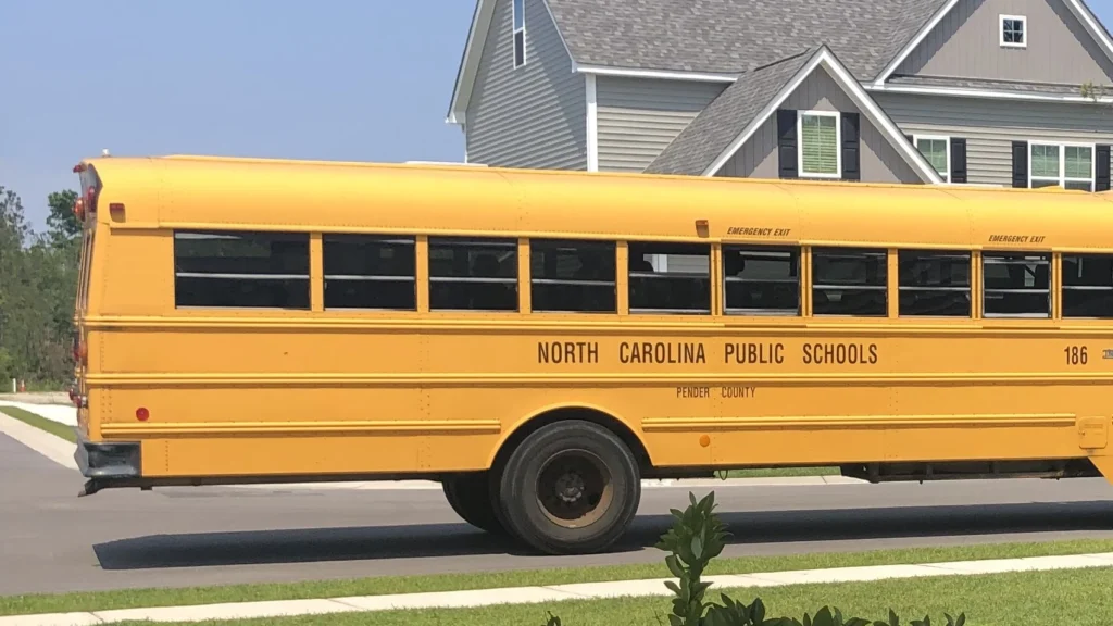 A Pender County Schools bus stopped on a residential street in front of newly built two-story homes.