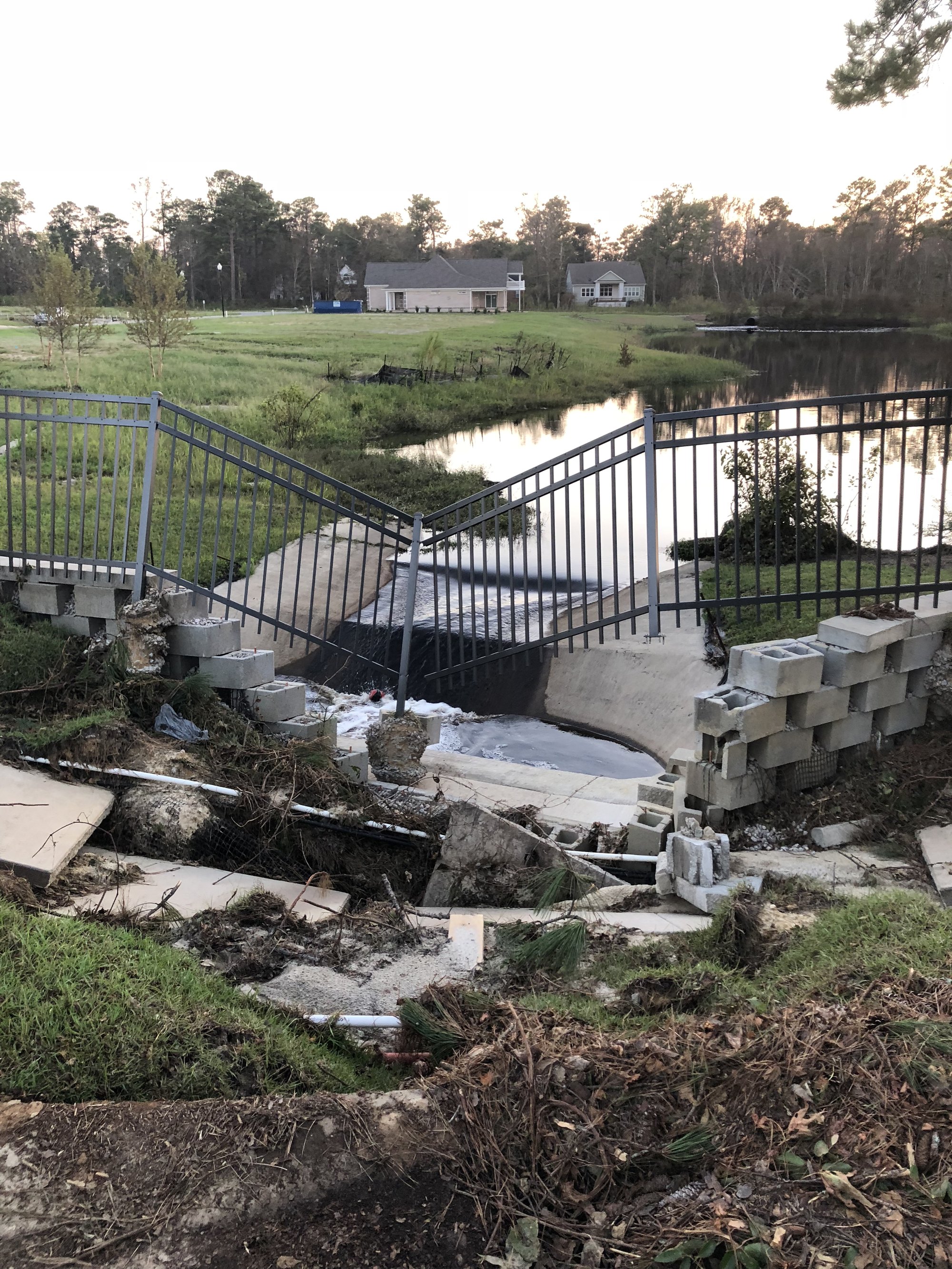 Undermined sidewalk, collapsed block wall and hanging fence at the Wyndwater spillway, September 2018