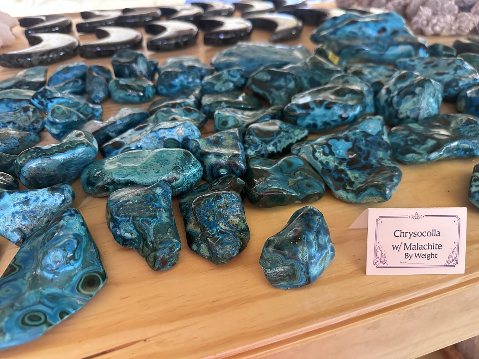 Polished slices of blue-green chrysocolla with malachite laid out on a pine table