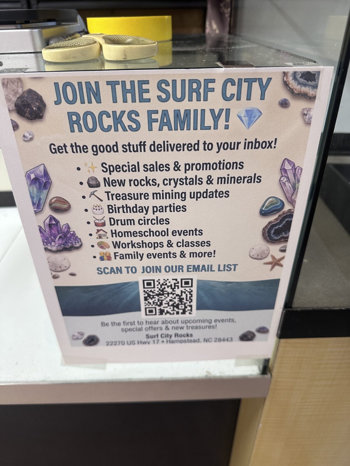 A printed sign at the register reading Join the Surf City Rocks Family, listing birthday parties, drum circles, homeschool events, workshops and classes, with a QR code for the email list