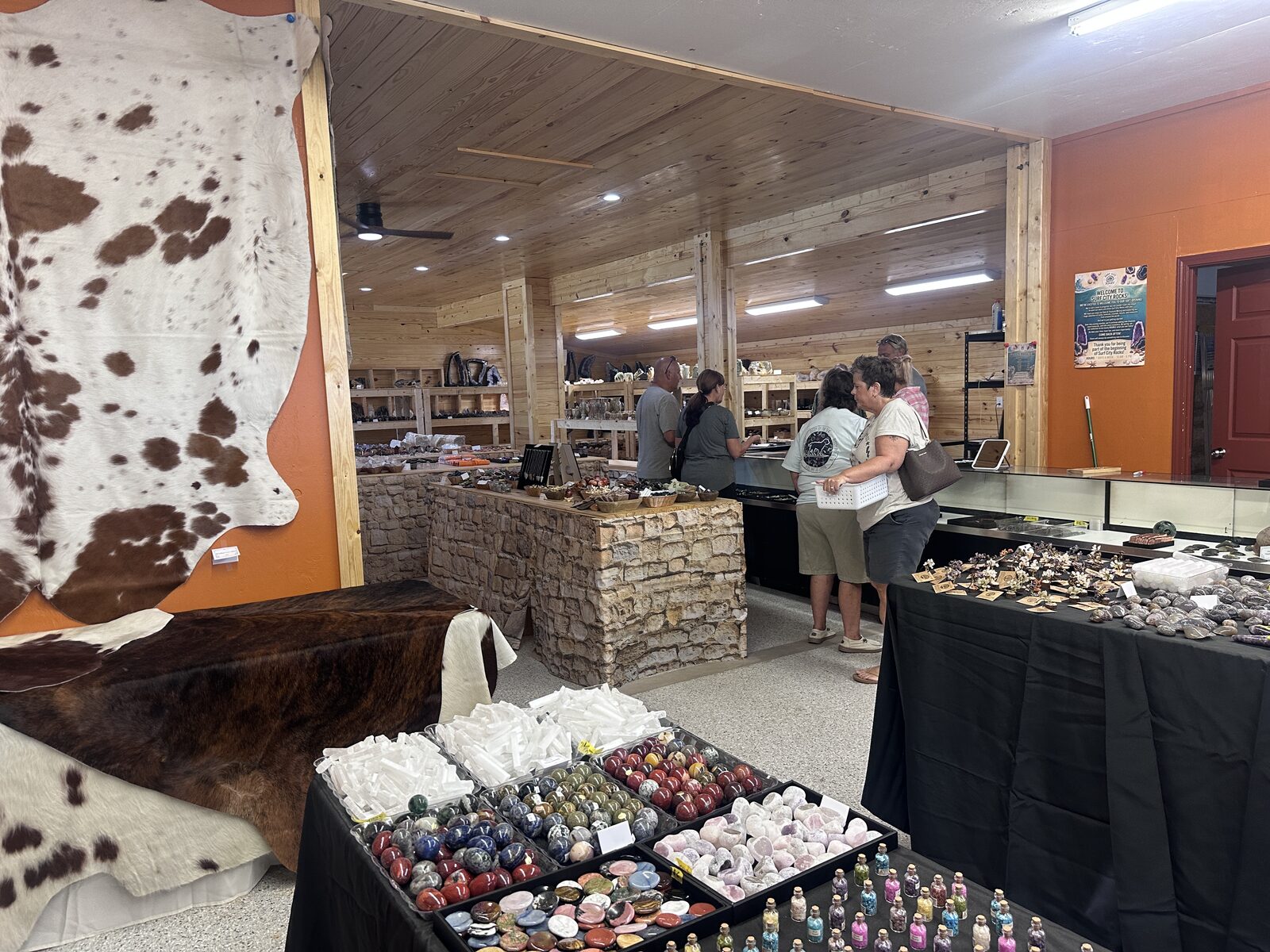Interior of Surf City Rocks on opening morning, with customers at a glass counter, open pine shelving, cowhides on an orange wall and tables of polished spheres in the foreground