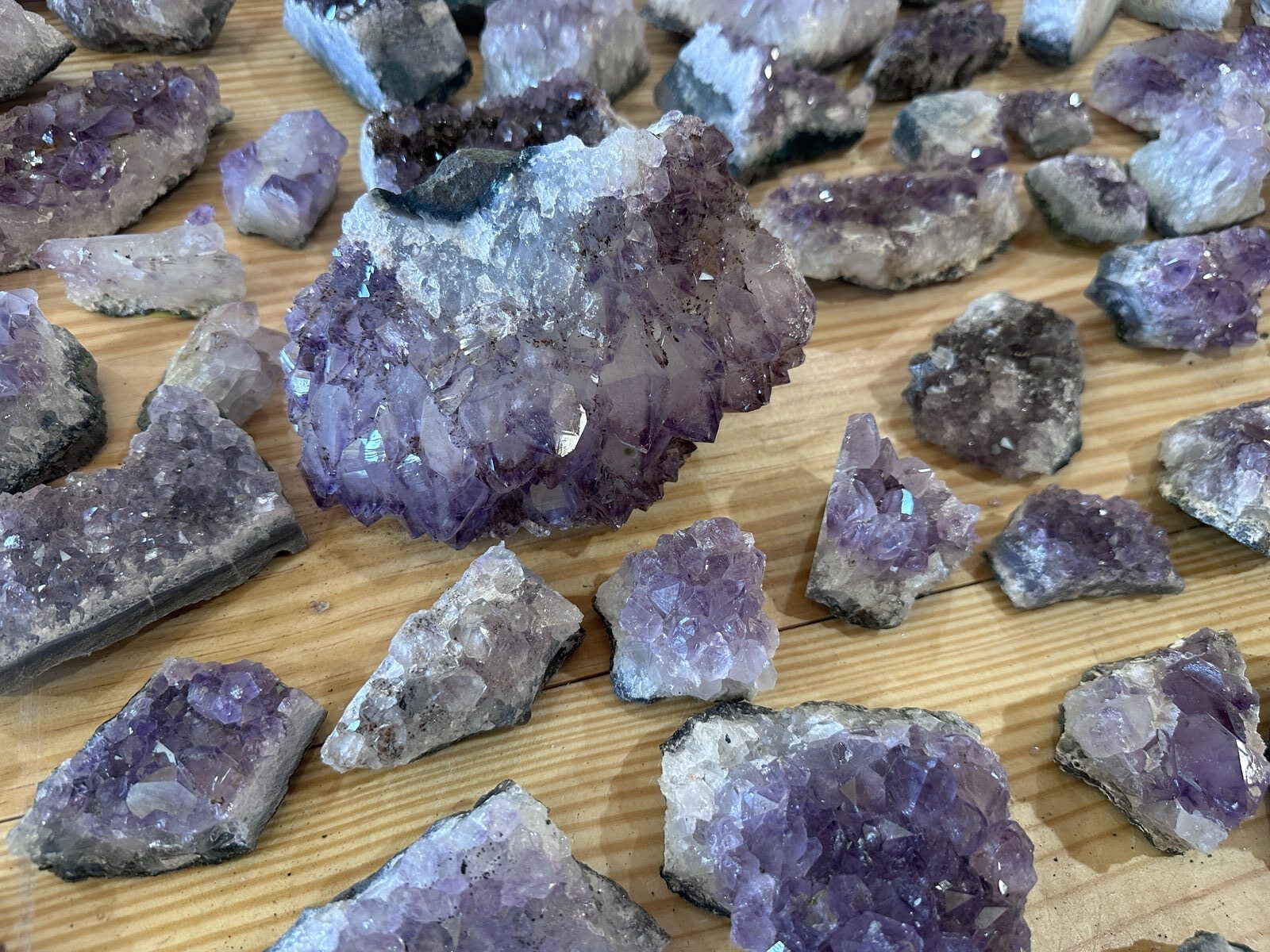 Dozens of amethyst cluster pieces arranged in rows on a pine table