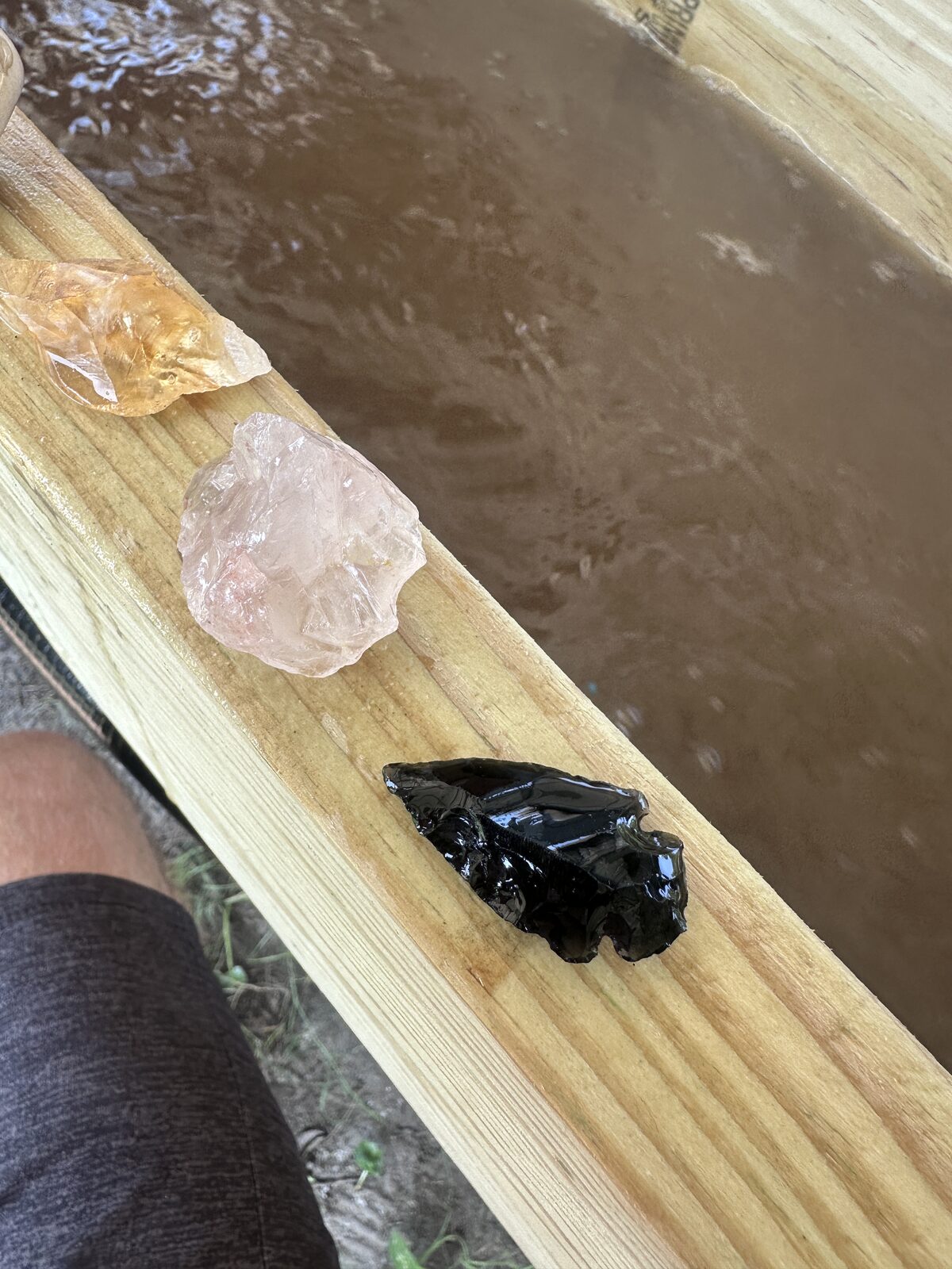 A rough citrine point, a piece of rose quartz and a black obsidian arrowhead on the sluice rail