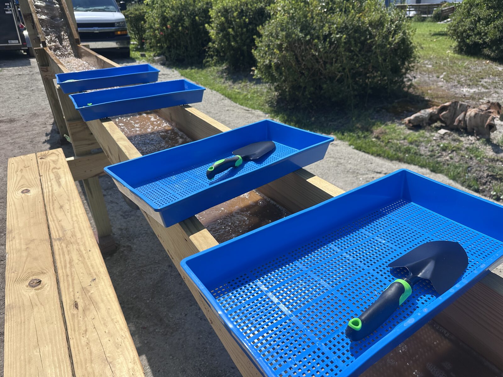 A row of blue sifting screens with trowels lined up along the wooden sluice trough